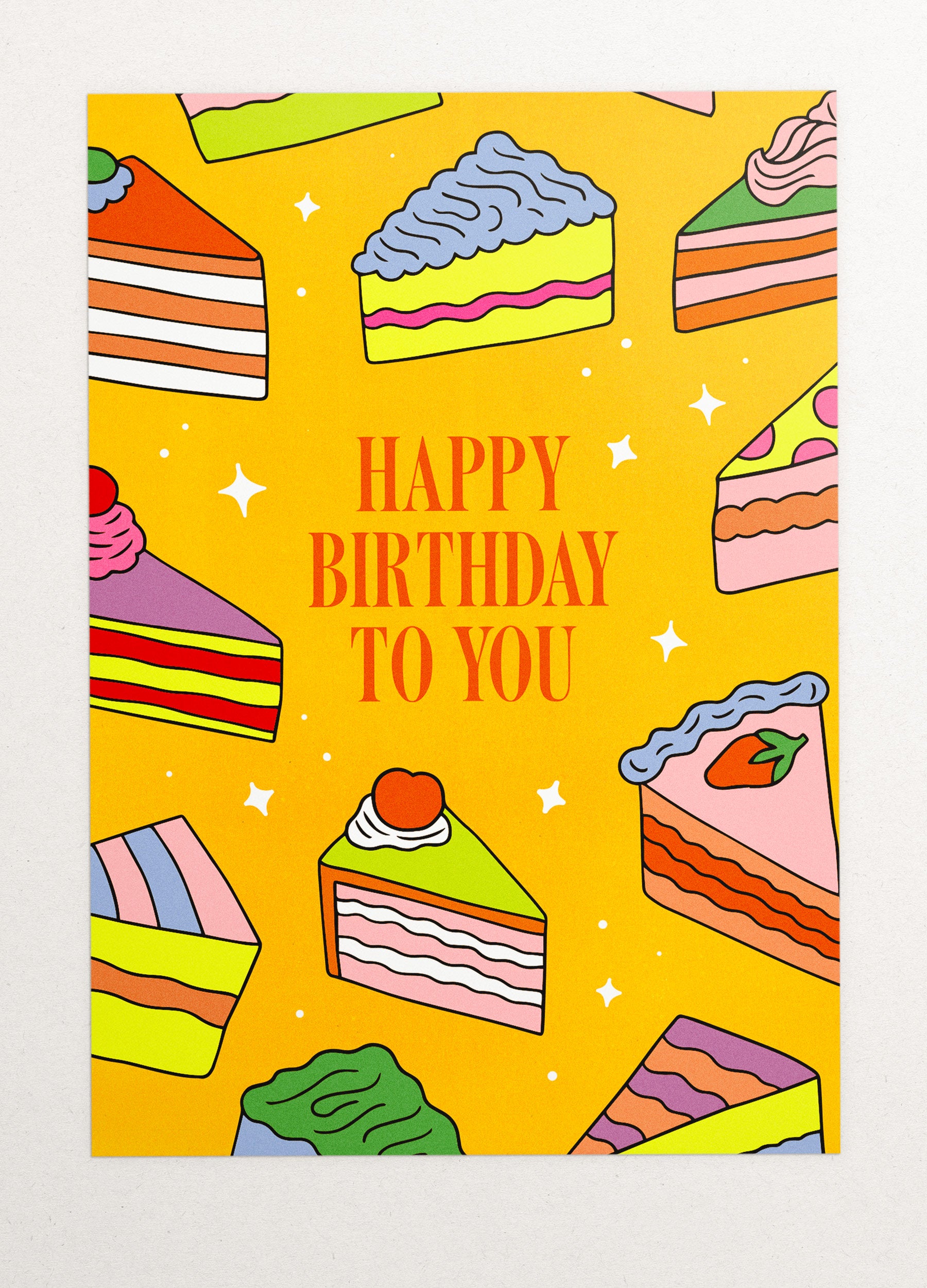 This is an image of a greeting card by Kiosk, that is illustrated by Georgia Perry. The card has a yellow background and illustrations of different types of cake slices scattered across the background. The cakes are in different colors and styles, including pink, green, and orange. The text on the card reads “Happy Birthday to You” in white letters. There are also small white stars scattered across the background.