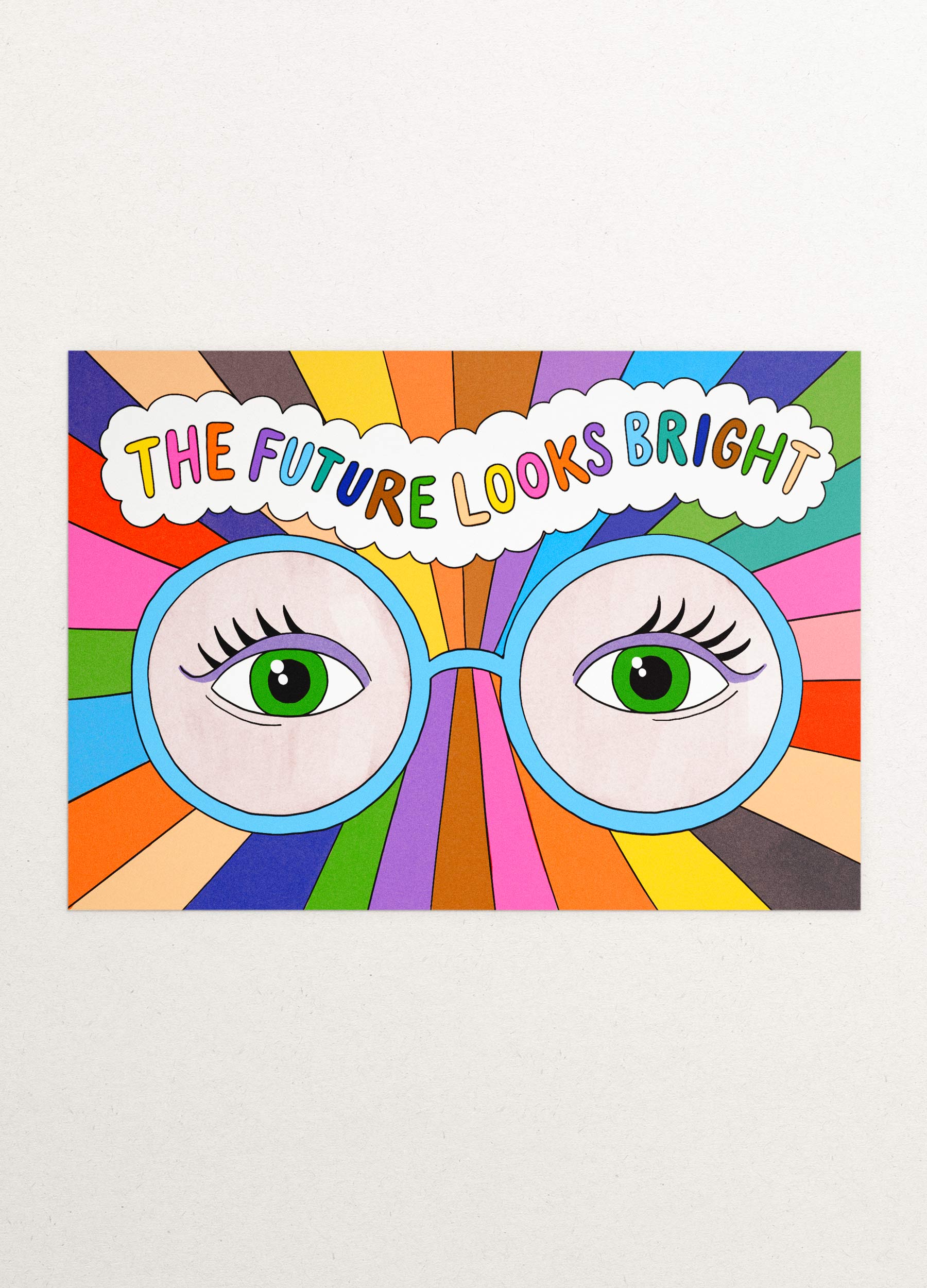 This is an image of a greeting card by Kiosk, that is illustrated by Georgia Perry. The card has an illustration of a pair of green eyes with colorful rays emanating from them. The rays are in various colors such as orange, pink, blue, green, and yellow. Above the eyes, there is a cloud with the text “The future looks bright” written in blue. The background is white and the illustration has a cartoon-like style.